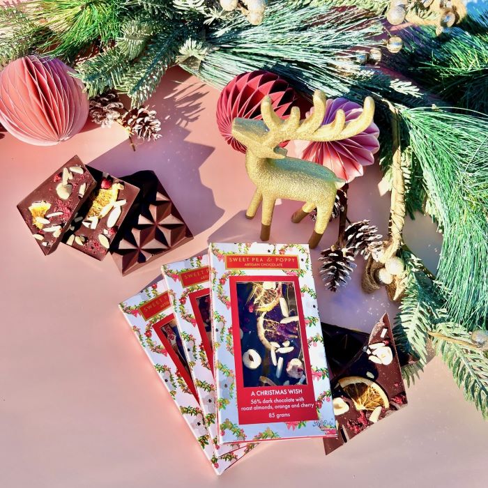 Chocolate bars with festive packaging and Christmas decorations on a pink surface