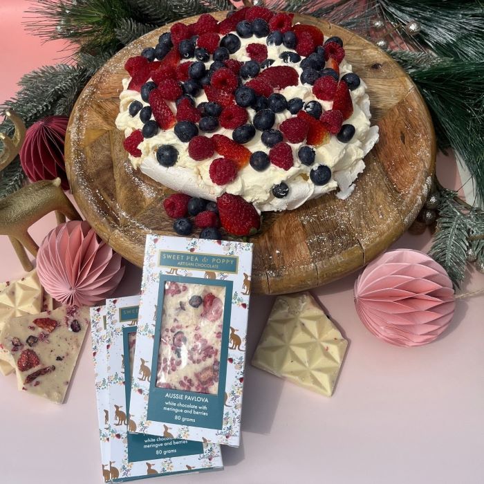 Decorative pavlova cake with berries on a wooden board, surrounded by chocolate bars and a product packaging.