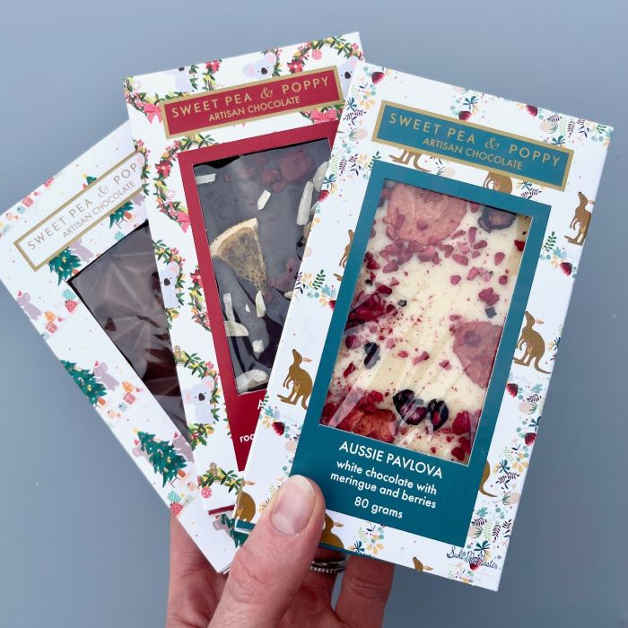Hand holding Sweet Pea & Poppy artisan chocolate bars with a focus on 'Aussie Pavlova' flavor.