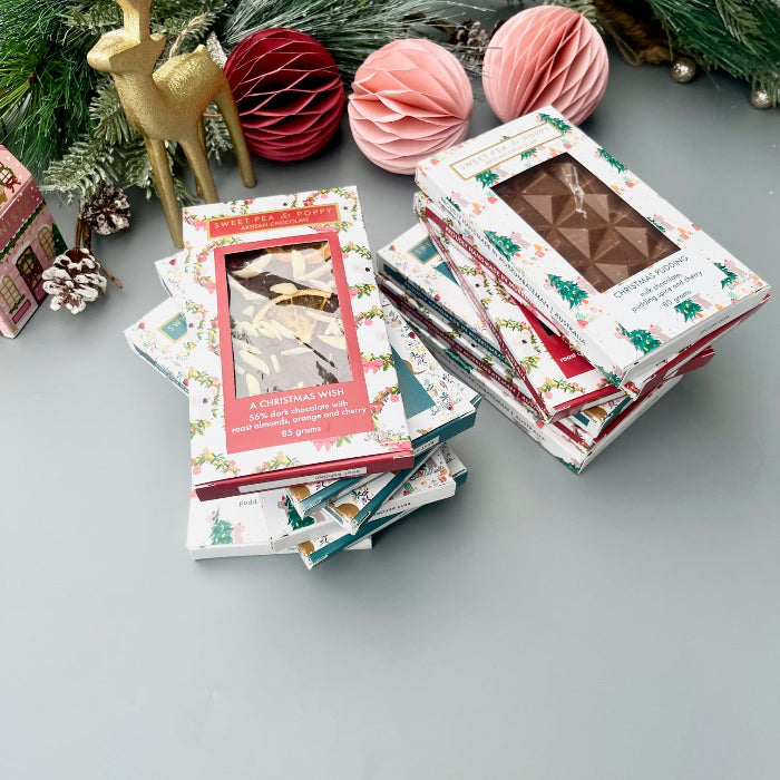 Stack of Christmas-themed chocolate bars on a gray surface with decorative items in the background.