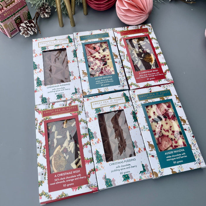 Chocolate bars packaged with Christmas-themed design on a gray surface with decorative items.