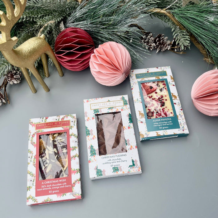 Three chocolate bars with Christmas-themed covers on a gray surface with decorative elements.
