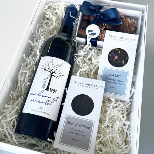 A gift box with red wine, boxed chocolate and two small chocolate bars