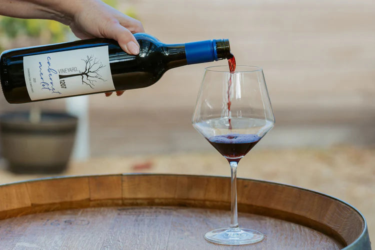 Red wine being poured from a bottle into a glass on a wooden barrel.