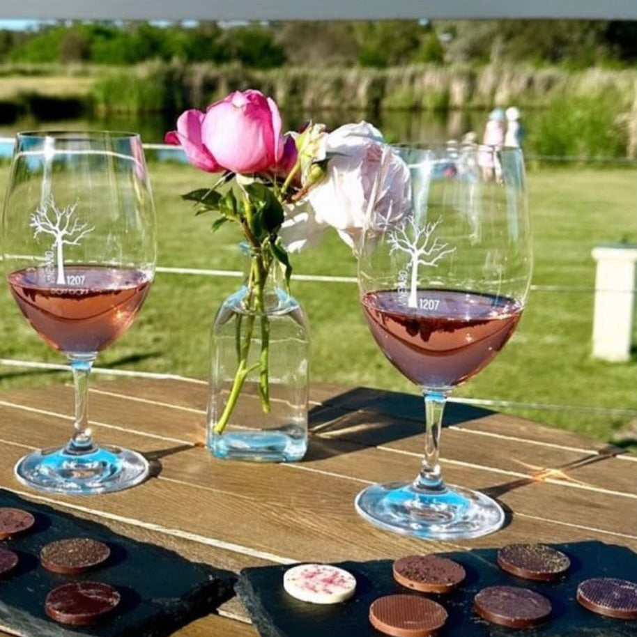 Two glasses of pink wine with a vase of flowers on a wooden table outdoors.