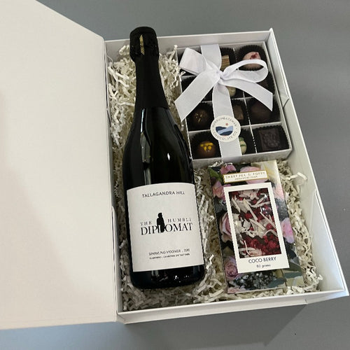 A gift hamper box with sparkling wine, boxed chocolates and a chocolate bar